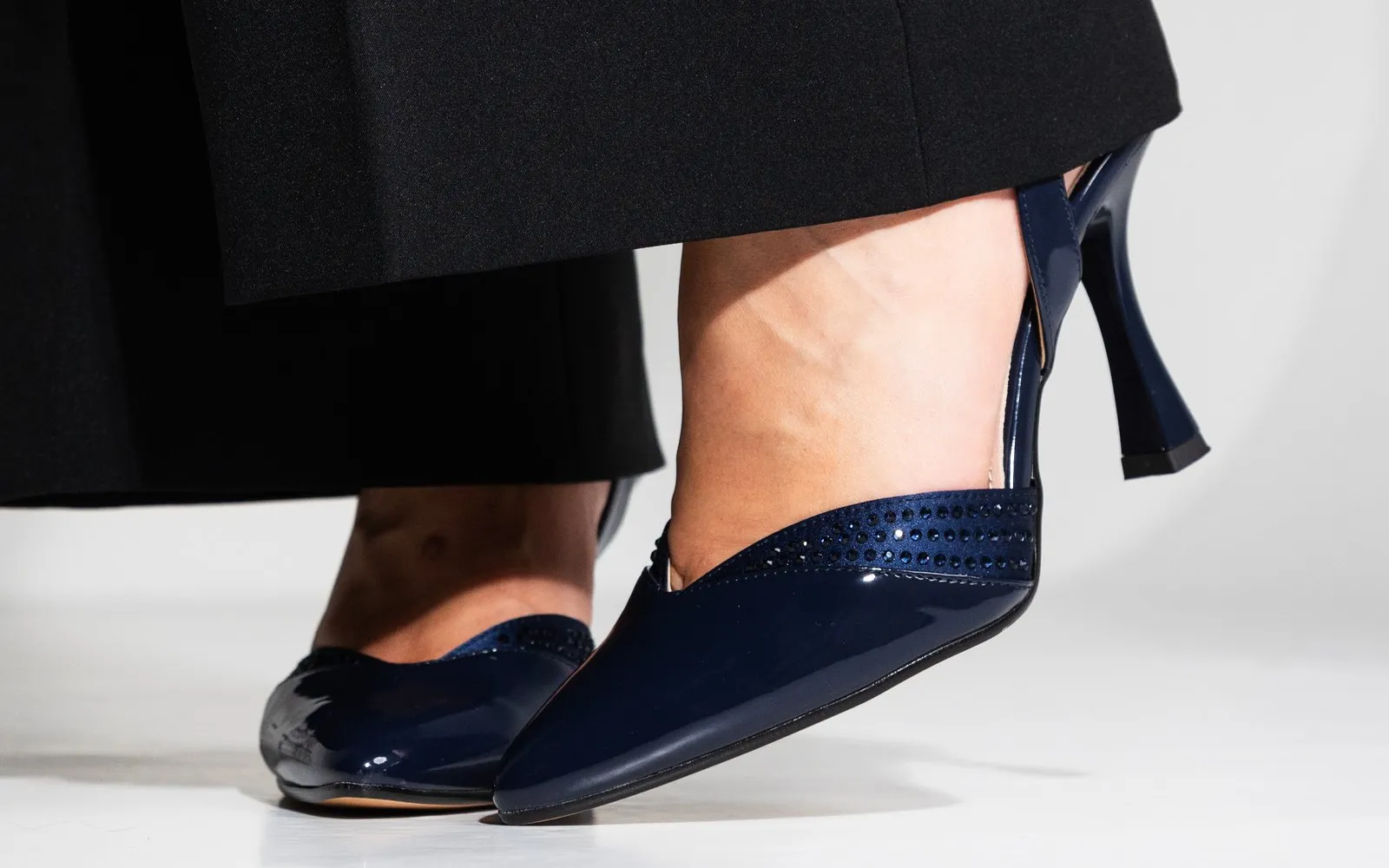 Slingback Gelsomina in vernice blu notte sotto un pantalone nero, in passo