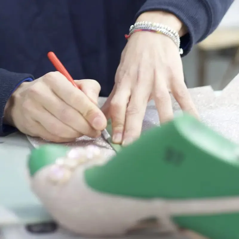 Le mani di un'artigiana segnano con la penna il taglio di un materiale glitter accanto a una forma verde