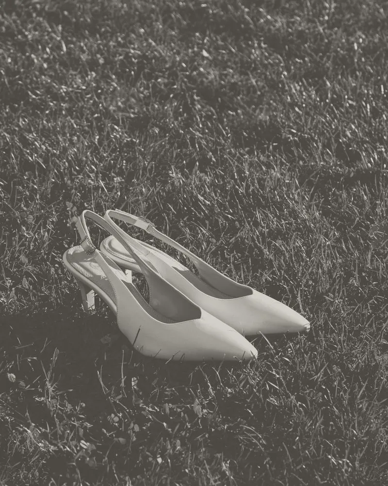Un paio di slingback da sposa in raso appoggiato sull'erba: foto in bianco e nero