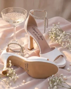 Coppia di sandali gioiello da sposa Ortensia in raso bianco con i nomi Chiara e Luca e la data 18-06-2027 sul sottopiede e sulla suola, «Made in Italy» e numero in oro: immagine di presentazione
