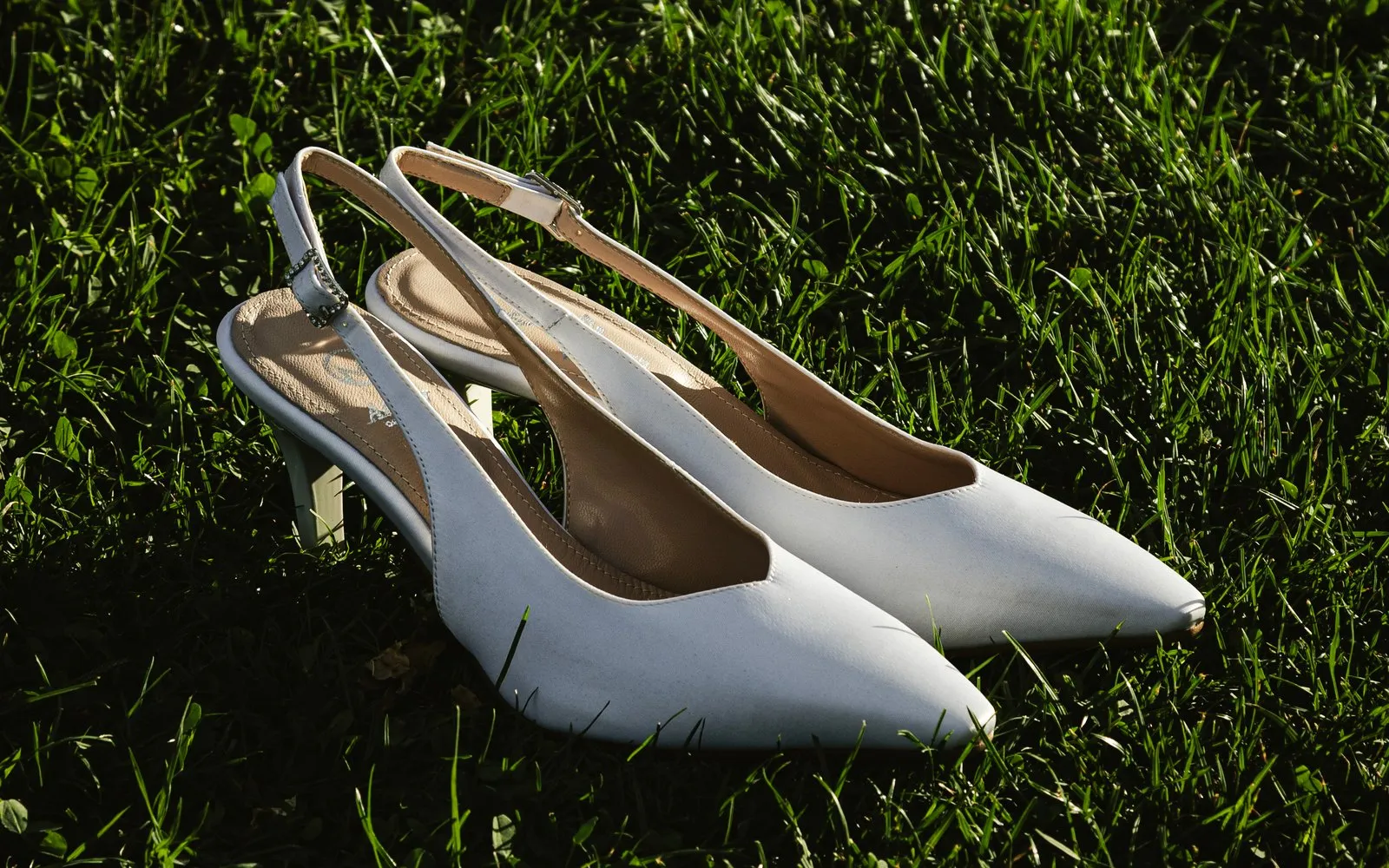 Un paio di slingback da sposa appoggiate sull'erba, in luce radente