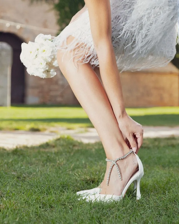 Una sposa allaccia la catenella di strass del sandalo Mimosa Sposa, sul prato